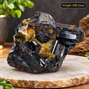 Könnte beinhalten: Ein rohes schwarzes Turmalin-Kristallcluster mit länglichen, gestreiften schwarzen Mineralformationen, die mit goldbraunen Matrixbereichen durchsetzt sind. Das Exemplar hat ein Gesamtgewicht von 340 Gramm, wie im Bildtext angegeben.
