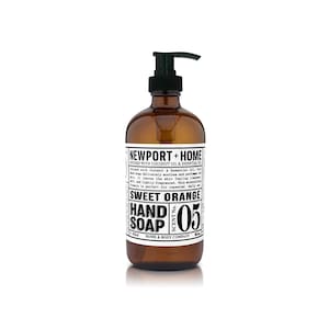 May include: A brown glass bottle of hand soap with a black pump dispenser. The label reads "NEWPORT + HOME" and "SWEET ORANGE HAND SOAP SCENT No. 05".