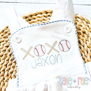 May include: White baby onesie with blue and white gingham trim. The onesie has a baseball-themed embroidery design with the text "XOXO Jaxon" and two baseballs with red stitching.