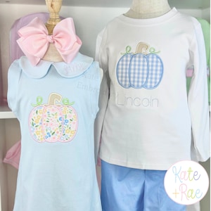 May include: A light blue sleeveless dress with a floral pumpkin appliqué and a pink hair bow, alongside a white long-sleeve shirt with a blue gingham pumpkin appliqué and blue shorts. The names Lilly and Lincoln are embroidered on the garments.