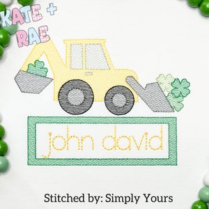 May include: A yellow toy construction vehicle with a green shamrock design. The vehicle is holding a scoop of green shamrocks. The text "john david" is stitched in a green frame below the vehicle.