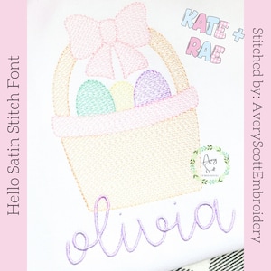 Puede incluir: Un dise&ntilde;o de bordado que muestra una cesta color canela con un lazo rosa grande, conteniendo tres huevos pastel en turquesa, amarillo y morado. El nombre "olivia" est&aacute; bordado en cursiva morada debajo. Incluye el texto "KATE + RAE" y "Hello Satin Stitch Font".