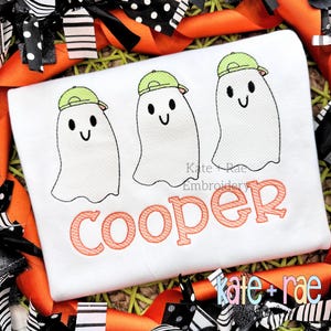 May include: White embroidered shirt with three ghosts wearing green baseball caps and the name "cooper" in orange lettering.