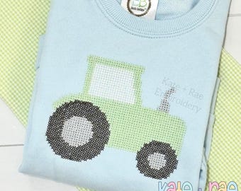 May include: A light blue sweatshirt featuring a green tractor design. The tractor has black and white wheels and a white cabin. The text "Kate + Rae Embroidery" is printed on the sweatshirt.