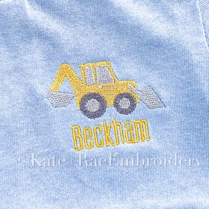 May include: Light blue baby outfit with an embroidered yellow and gray construction digger. The name "Beckham" is embroidered in yellow below the digger. The text "Kate Rae Embroidery" is embroidered below the name.