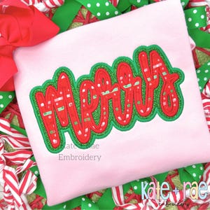 May include: A pink shirt with a red and green "Merry" embroidered on the front. The embroidery has a striped pattern and a glittery finish.