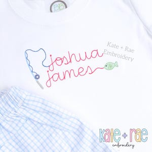May include: White t-shirt with red embroidery of the names "Joshua James" and a fishing line with a green fish. The text "Kate + Rae Embroidery" is also embroidered on the shirt.