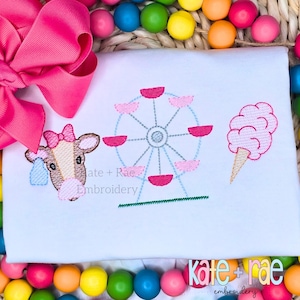 May include: Embroidered design on a white t-shirt featuring a brown cow with pink ears and a pink bow, a pink and blue Ferris wheel, and a pink cotton candy on a stick. The text "kate + rae embroidery" is at the bottom of the design.