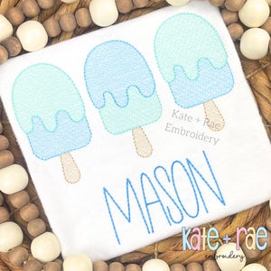 Puede incluir: Tres diseños de bordado de paletas de helado azules y azul claro con un efecto de goteo. El nombre "MASON" está bordado en azul debajo de las paletas de helado. El texto "Kate + Rae Embroidery" está bordado en negro debajo del nombre.