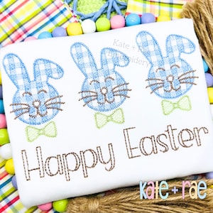 Puede incluir: Tela blanca con caras de conejitos bordadas en azul y verde y el texto "Feliz Pascua".