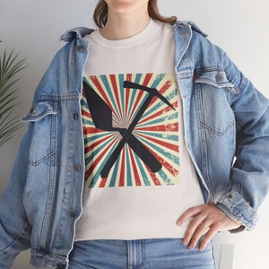 May include: White t-shirt with a graphic of a pickaxe and shovel crossed against a retro background of red, white, and blue rays. The shirt is worn with a denim jacket. The design has a distressed, vintage look.