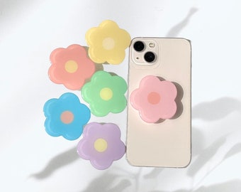 May include: Six colorful flower-shaped phone grips in various pastel colors, including pink, blue, yellow, green, and purple. The grips are attached to a white iPhone.