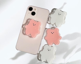 May include: Three phone grips in the shape of a cartoon bear. Two are pink and one is white. The phone grips have a simple smiling face.