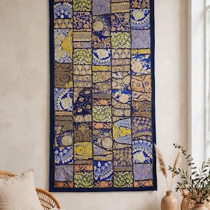 May include: A rectangular wall hanging featuring a patchwork design of various fabric squares in shades of deep blue, gold, and green. The textile displays intricate embroidery, metallic thread accents, and diverse floral and geometric patterns.