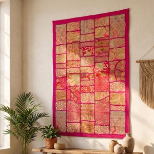 May include: A rectangular wall hanging featuring a patchwork design of vibrant hot pink and metallic gold fabric squares. The textile displays intricate floral and paisley patterns with embroidered details, finished with a solid hot pink border.