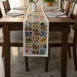 May include: A dining table set for six with a colorful patchwork table runner. The table is made of dark wood, and the chairs have light-colored seats. A white vase with flowers sits on the runner.