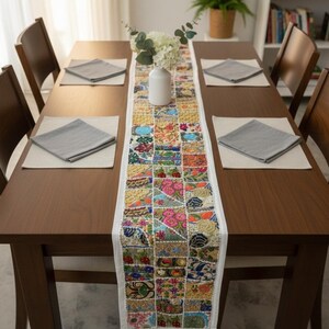 May include: A dining table set for six with a patchwork table runner. The runner has floral and geometric patterns in pink, blue, yellow, and green. The table is set with grey napkins and placemats. The table runner is approximately 180 cm long.