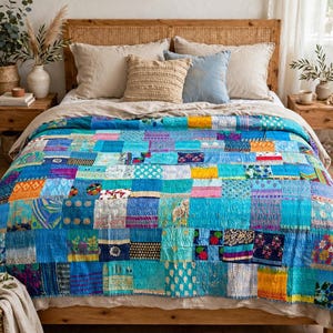May include: A patchwork quilt featuring a variety of blue, turquoise, and teal fabric squares with diverse patterns, floral prints, and textures. The quilt is layered over a bed with neutral-toned pillows and a light-colored linen bedspread.