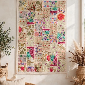 Op de afbeelding: Een rechthoekige wandhanger met een patchworkontwerp van diverse geborduurde stoffen vierkanten. Het textiel toont een veelheid aan bloemmotieven en ingewikkeld stikwerk in levendige kleuren zoals roze, groen, blauw en goud op een crèmekleurige basis.