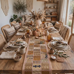 May include: A long rectangular table runner featuring a patchwork design of various golden, brown, and cream fabric squares with intricate embroidery and paisley patterns, centered on a wooden dining table set with ceramic plates and glassware.