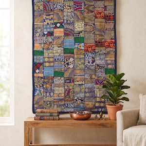Peut inclure: Une grande tenture murale textile en patchwork coloré, avec une bordure bleu foncé. Le textile est composé de nombreux patchs rectangulaires aux motifs et couleurs variés, notamment des bleus, des verts, des rouges et des ors. Accroché au-dessus d'un banc en bois.