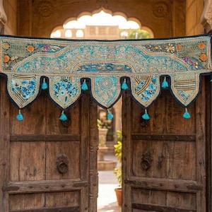May include: A decorative textile door hanging with a turquoise and black design. The hanging features floral patterns, tassels, and intricate embroidery. It is displayed over a set of wooden doors, adding a touch of bohemian style.