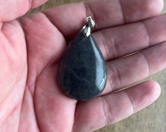 Puede incluir: Un colgante de color gris oscuro en forma de lágrima con un aro de plata.