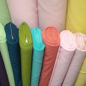May include: A collection of colorful fabric rolls in various shades, including brown, purple, green, teal, coral, pink, yellow, and white. The rolls are tightly wound, showcasing the different textures and colors of the fabric.