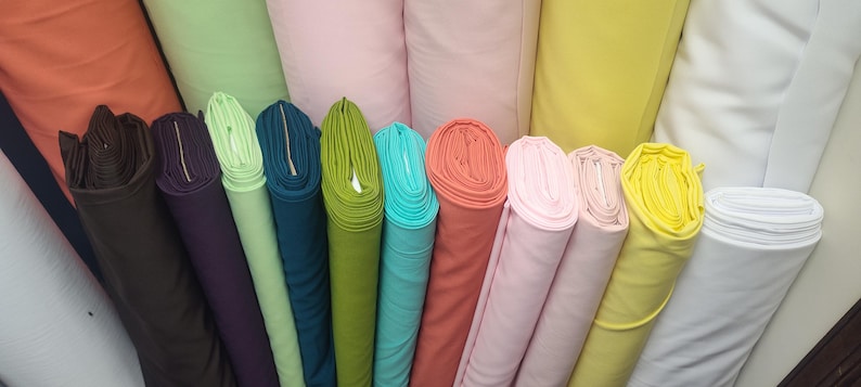 May include: A collection of colorful fabric rolls in various shades, including brown, purple, green, teal, coral, pink, yellow, and white. The rolls are tightly wound, showcasing the different textures and colors of the fabric.