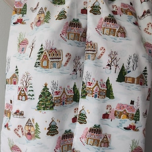 May include: White fabric scarf with a repeating pattern of gingerbread houses, candy canes, and Christmas trees. The houses are decorated with pink and brown icing and have white snow on the roofs. The trees are green and have white snow on the branches. The candy canes are red and white.