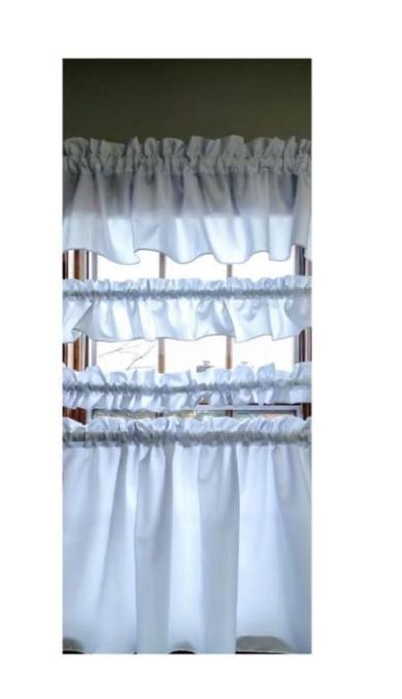 May include: White ruffled window curtains. The curtains are made of a soft, flowing fabric and are designed to add a touch of elegance to any room. The curtains are layered, with multiple tiers of ruffles.