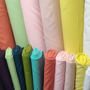 May include: A collection of fabric rolls in various colors, including green, pink, yellow, and teal. The rolls are tightly wound and stacked together, showcasing a variety of textiles for sewing and crafting projects.