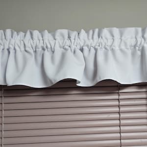 May include: White ruffled valance over a window with closed blinds. The valance is made of a soft, flowing fabric and is gathered at the top. The blinds are a light brown color.