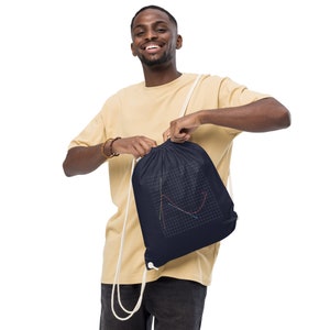 May include: Navy blue drawstring bag with a white cord. The bag displays a graph design in red, green, and white on a grid. The bag is held by a person.