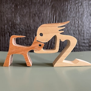 May include: Wooden figurine of a person kneeling and reaching out to a smaller wooden figurine of a dog. Both figurines are made of light brown wood.