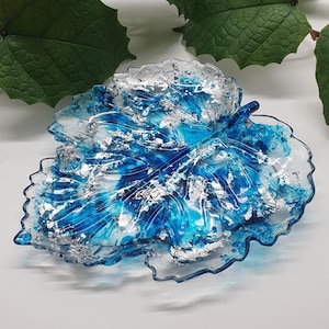 Könnte beinhalten: Eine blaue und silberne, blattförmige Schale aus Harz. Die Schale ist so gestaltet, dass sie einem echten Blatt ähnelt, mit Adern und einer strukturierten Oberfläche. Die Schale ist ideal für die Aufbewahrung von kleinen Gegenständen wie Schmuck oder Schlüssel.