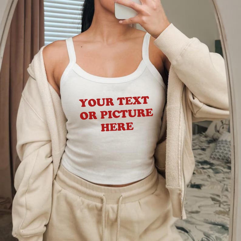 May include: White tank top with the text "YOUR TEXT OR PICTURE HERE" in red. The tank top is worn with a beige zip-up hoodie and matching sweatpants. The image is taken in front of a mirror.