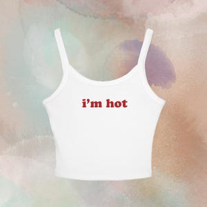 May include: White tank top with thin straps and the text "i'm hot" in red. The top is a casual style, suitable for warm weather. The background has a watercolor effect with shades of pink, green, and purple.