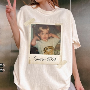 May include: Off-white t-shirt with a Polaroid-style photo of a child attached. The photo has the text "Senior 2026" beneath it. The child in the photo is wearing a shirt with the words "Pittsburgh Pirates".