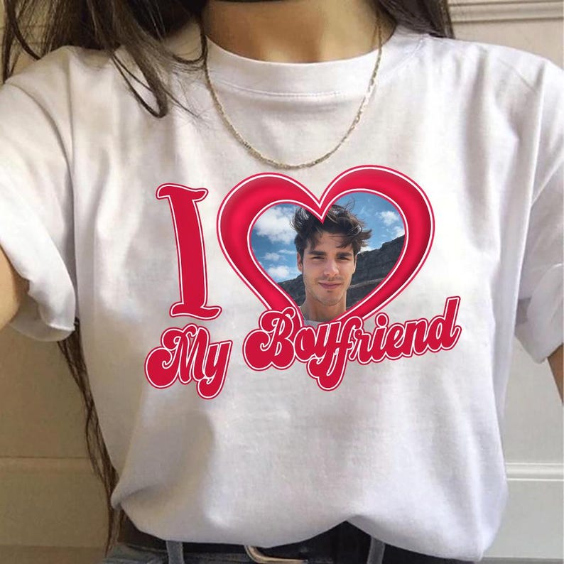 May include: White t-shirt with a red heart graphic containing a photo of a man. The words "I" and "My Boyfriend" are in red script. The shirt is a casual style.