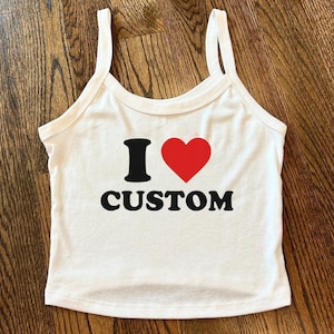 May include: White tank top with black text that reads "I ♥ CUSTOM" with a red heart symbol. The top has thin straps and a scoop neckline.