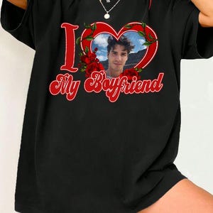 May include: Black t-shirt with a red heart-shaped graphic containing a photo of a person. The words "I" and "My Boyfriend" are in red script. Red roses and green leaves surround the heart.