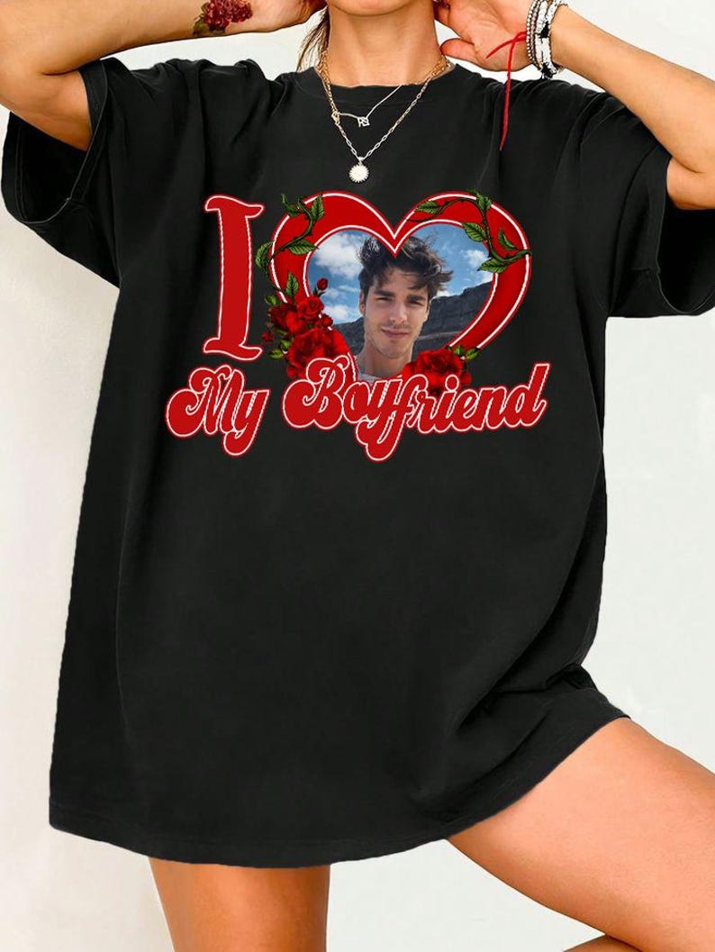 May include: Black t-shirt with a red heart-shaped graphic containing a photo of a person. The words "I" and "My Boyfriend" are in red script. Red roses and green leaves surround the heart.