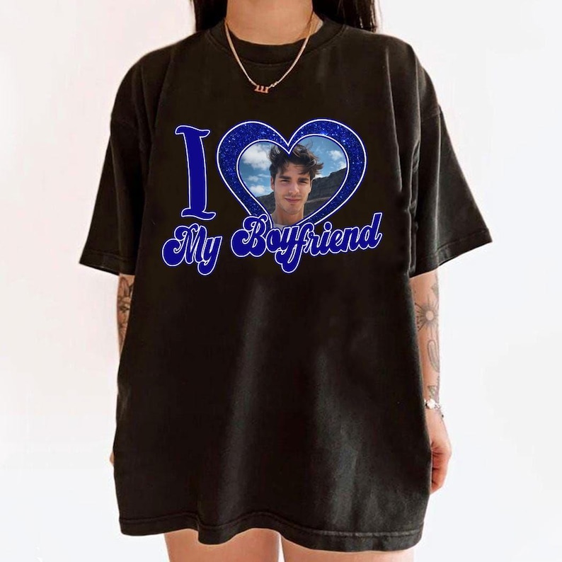 May include: Black t-shirt with a blue heart graphic containing a photo of a person. The text "I My Boyfriend" is written in blue script below the heart. The shirt has short sleeves and a crew neck.