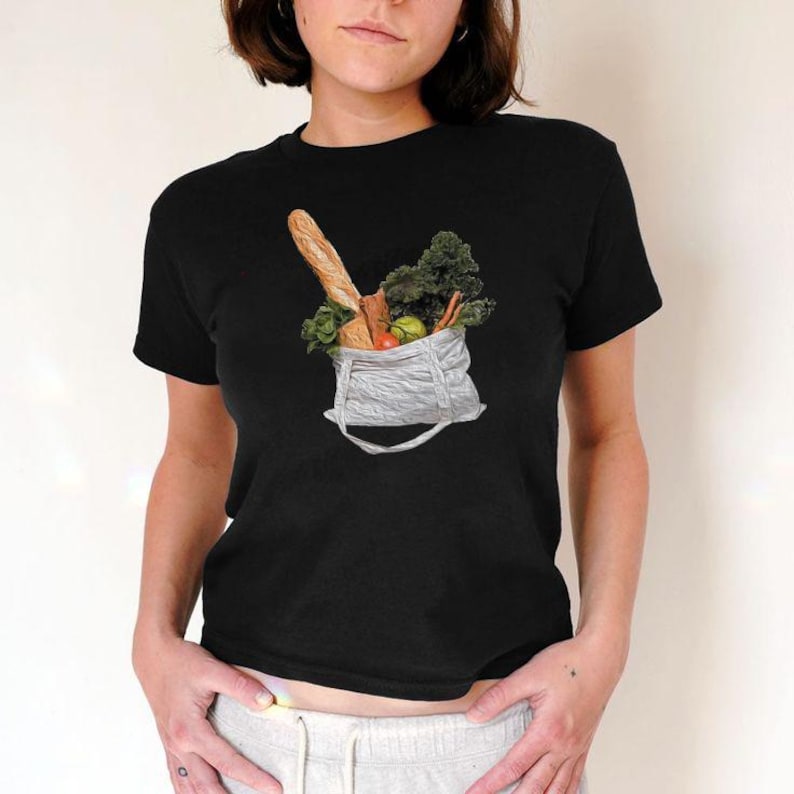 May include: A black t-shirt with a graphic of a reusable shopping bag filled with groceries, including a baguette, vegetables, and fruit.