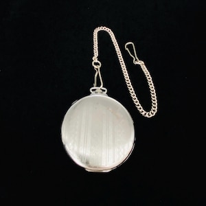 May include: A silver pocket watch with a matching chain and clasp. The watch has a round face with vertical lines and a shiny finish. The chain is attached to the top of the watch.