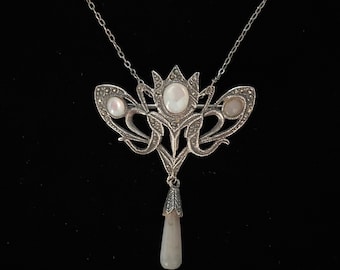 Op de afbeelding: Een zilveren ketting met een hanger in de vorm van een gestileerd bloemmotief met drie parelmoerstenen. De hanger is bevestigd aan een delicate zilveren ketting.