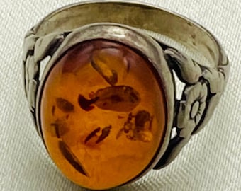 May include: A silver ring with an oval amber stone set in a floral design.