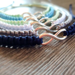Puede incluir: Un conjunto de cinco pulseras de amistad coloridas con un dije de infinito plateado. Las pulseras están hechas de cuerda tejida y vienen en tonos de azul, verde, blanco y gris.