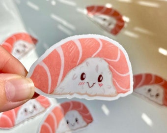 May include: A set of six pink and white sushi stickers with cute faces. The stickers are arranged in a semi-circle on a white surface.